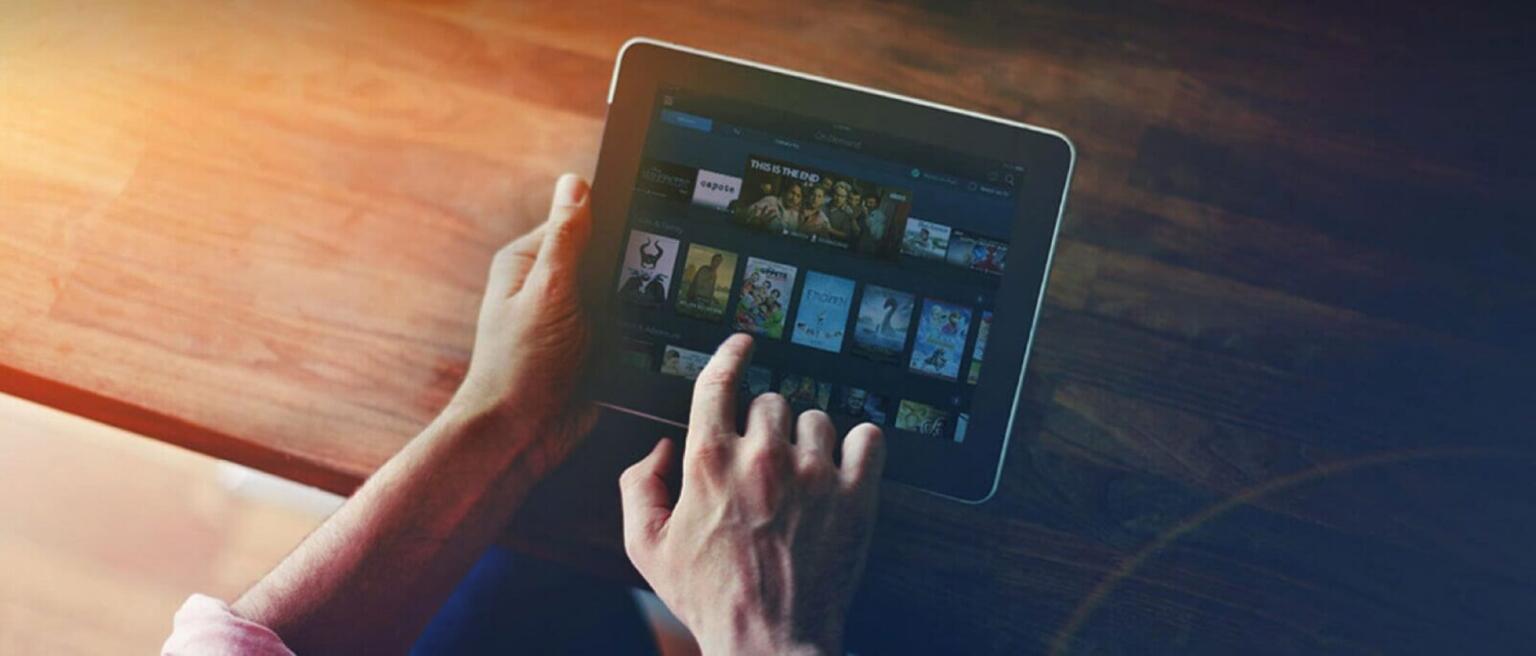 Close up of hands holding a tablet, pointing to entertainment choices on the screen.