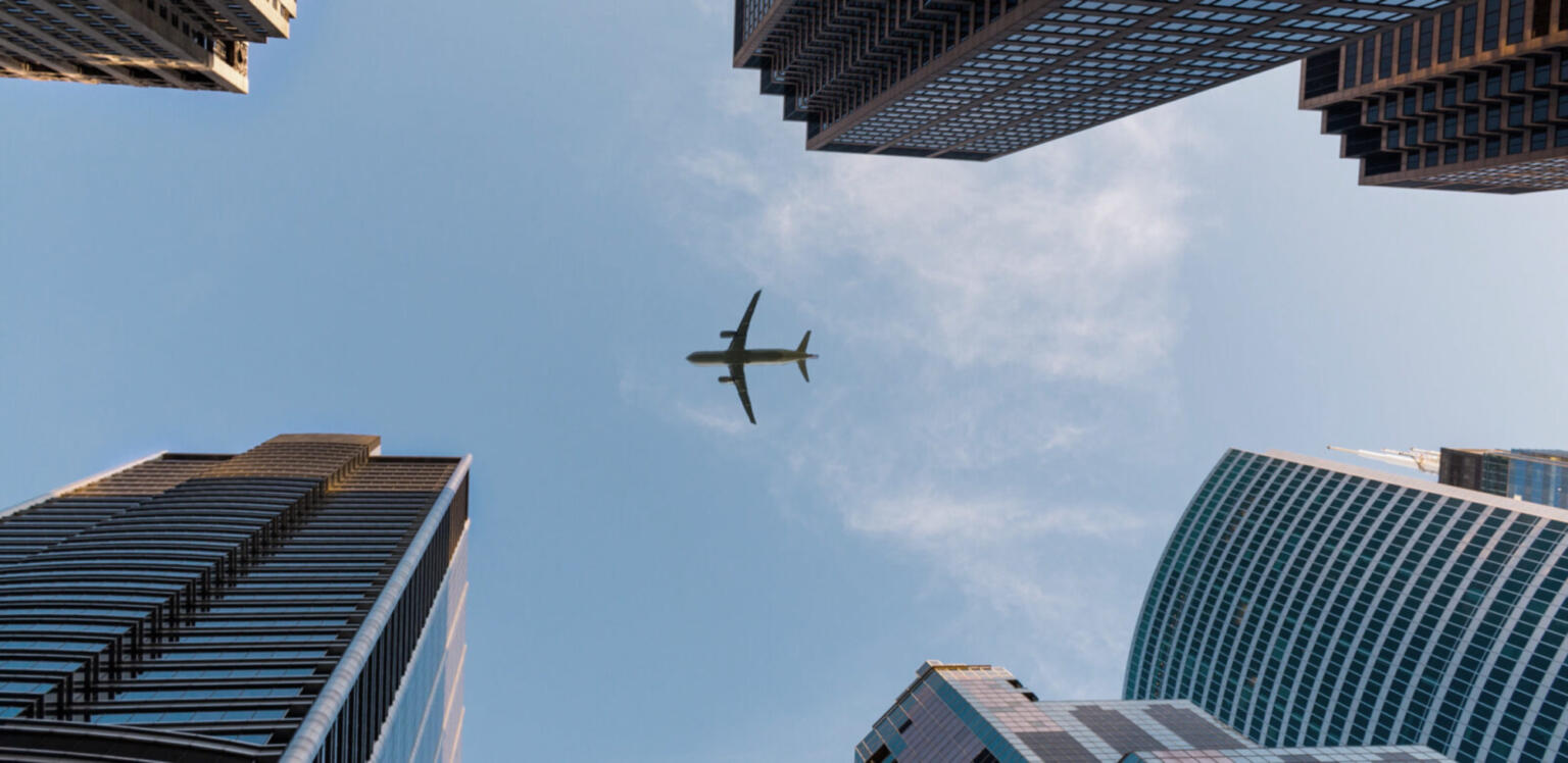 Looking straight up between buildings to see an airplane flying overhead.