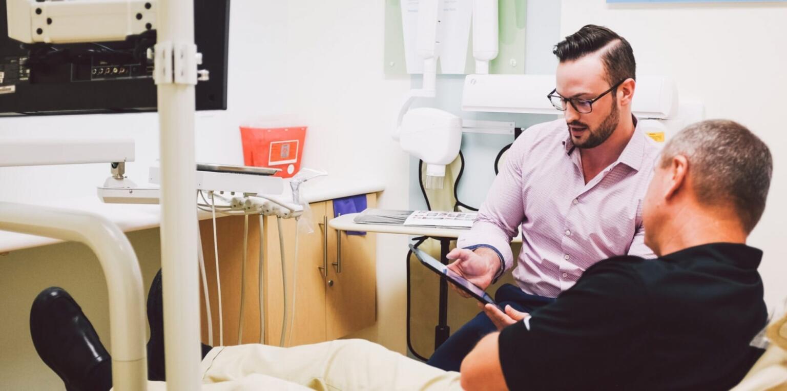 Dentist and patient reviewing treatment options on handheld tablet.
