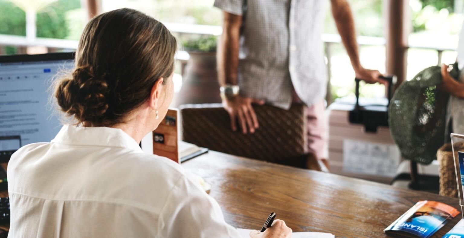A person standing with hand on a chair checking into a hotel.