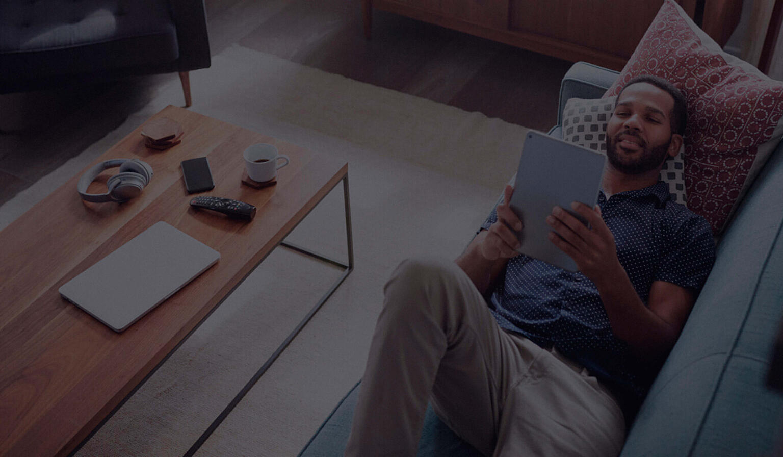 Man lounging on a couch, watching something on his tablet.