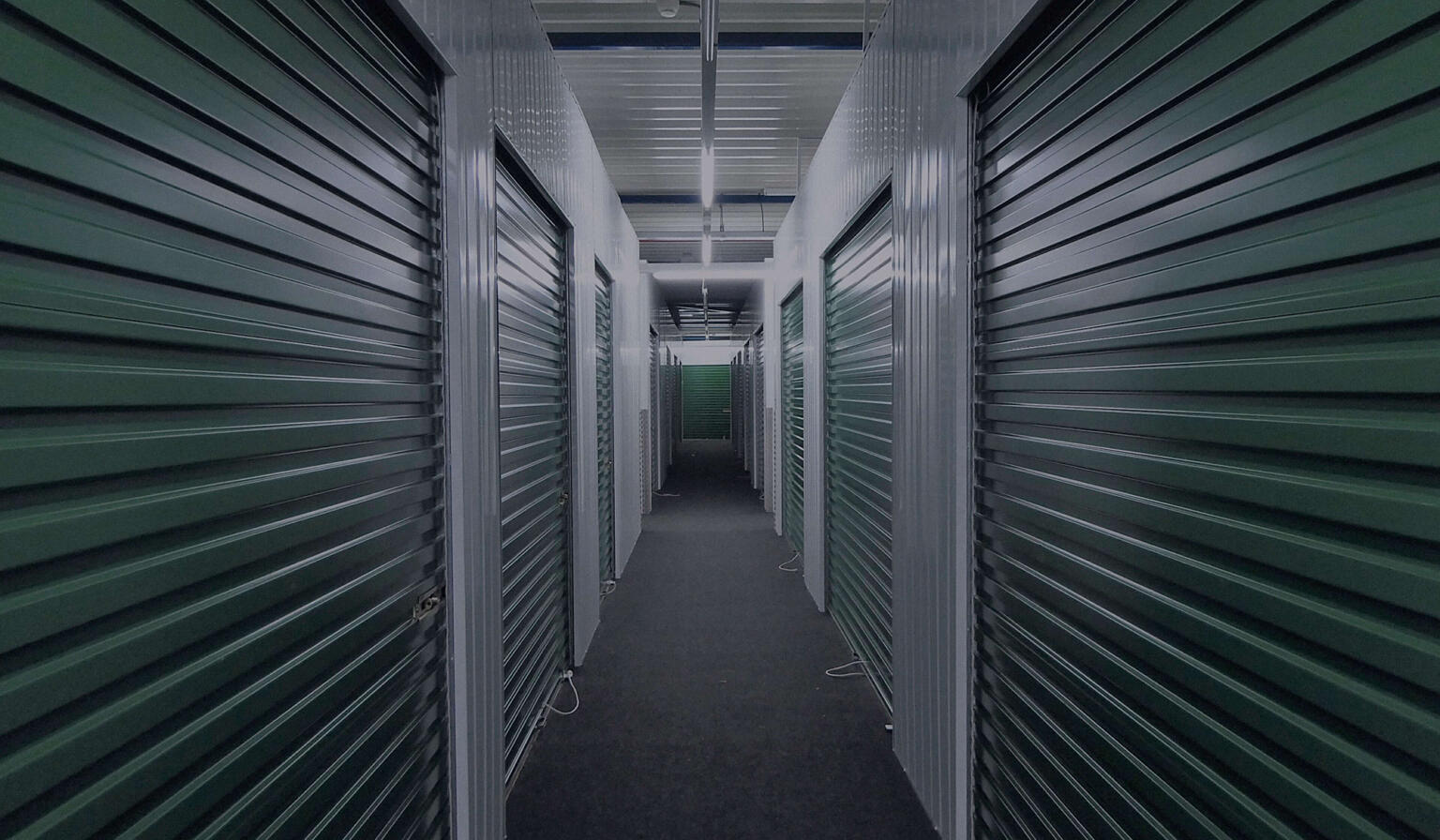 Green metal doors lining a long hallway in a storage facility.