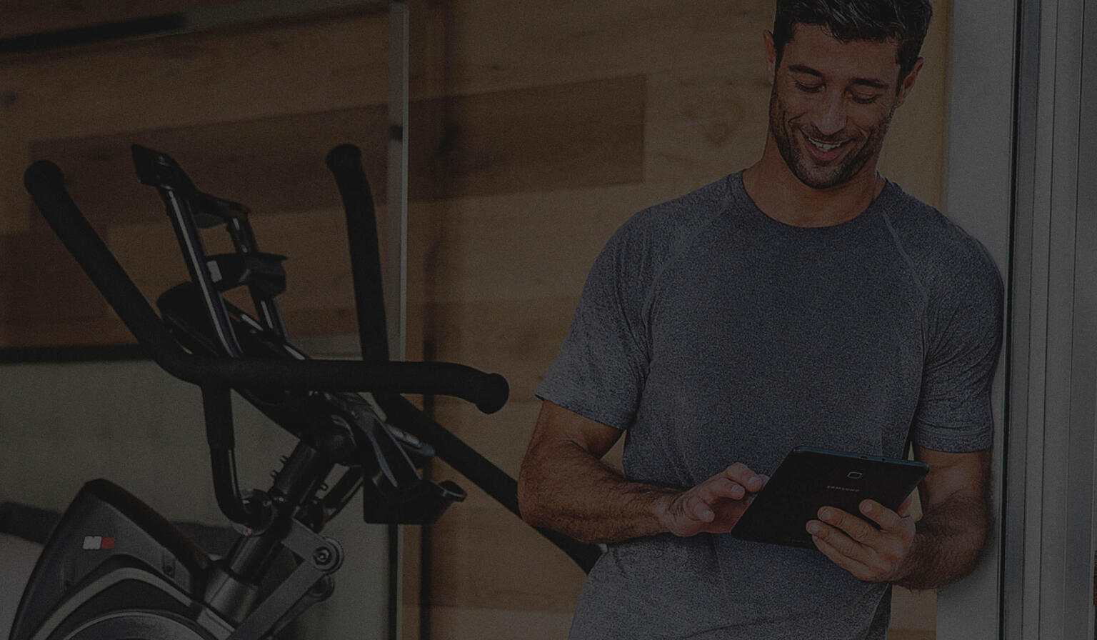 Man tapping at a tablet with exercise equipment in the background.